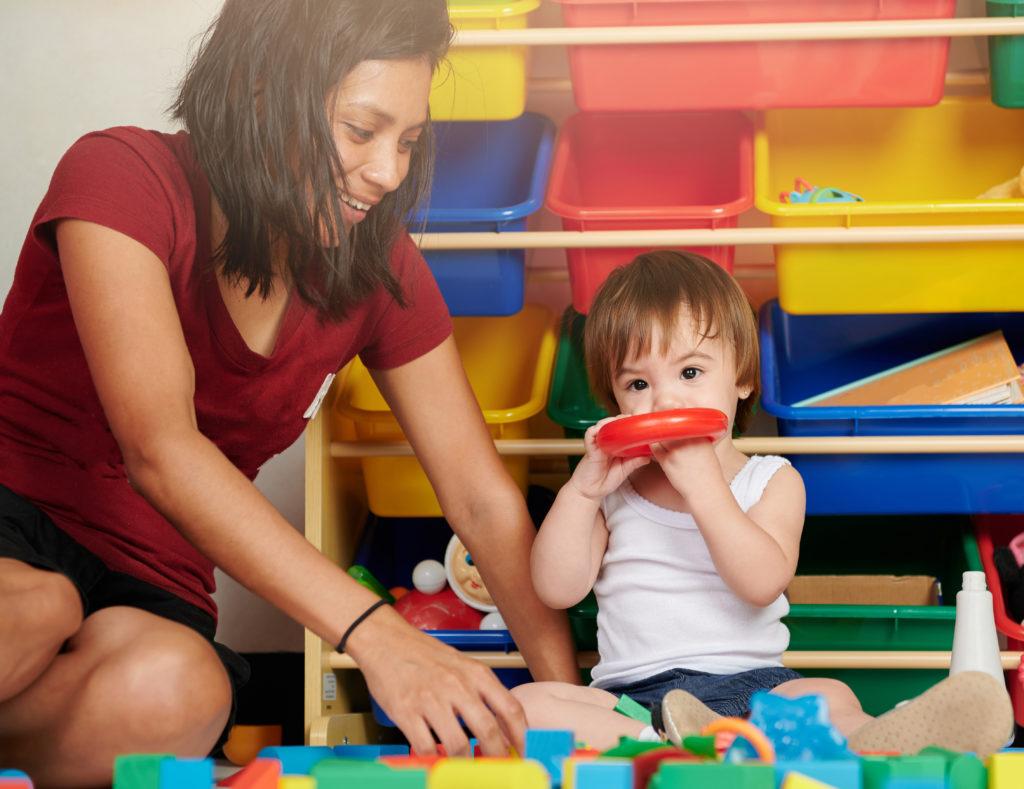 Adult woman and child play together on colorful toys background.